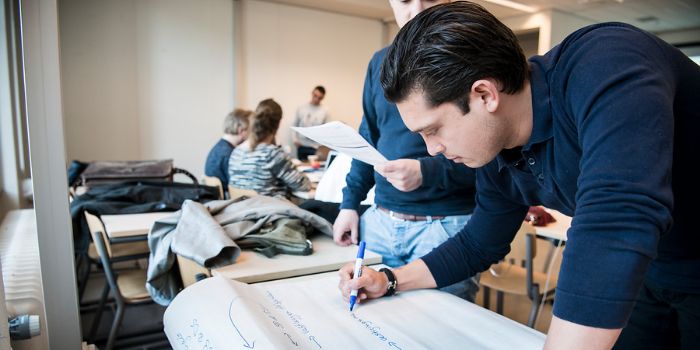 Student buigt over een groot vel papier en schrijft daarop met een viltstift