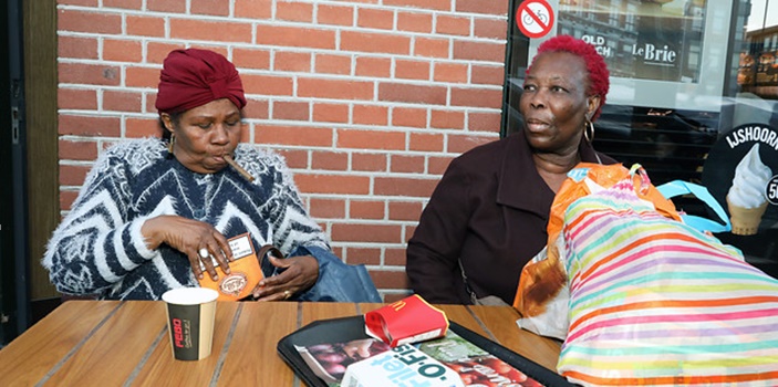 Twee oudere dames op terras in de Bijlmer, een steekt sigaar op