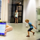 Meisje houdt telefoon met SIMBA-app vast, kinderen voetballen en springen op trampoline